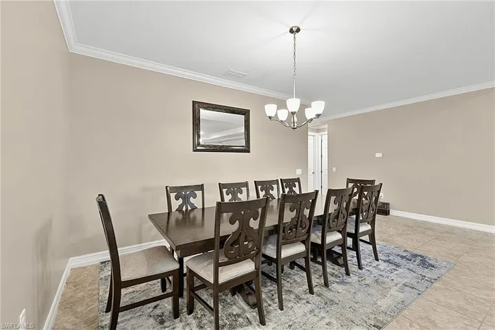 Spacious dining area featuring neutral wall tones, crown molding, a brushed nickel chandelier with frosted glass shades, tile flooring, and white baseboards