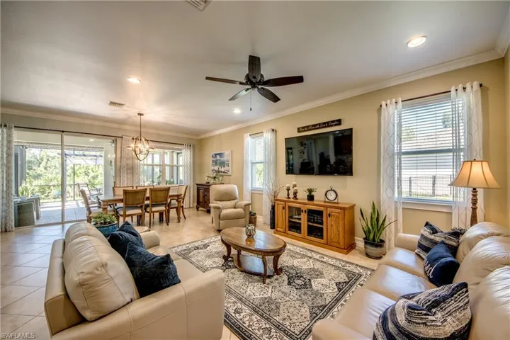 Living room with ceiling fan with notable chandelier, crown molding, and a wealth of natural light