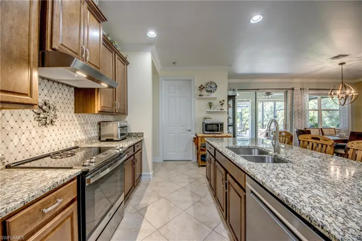 Kitchen with hanging light fixtures, light stone countertops, stainless steel appliances, sink, and light tile floors
