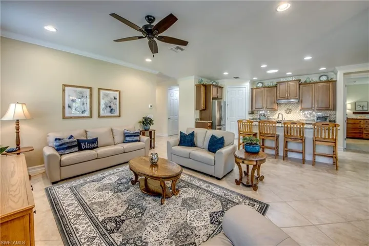 Living room with ceiling fan, light tile floors, and ornamental molding
