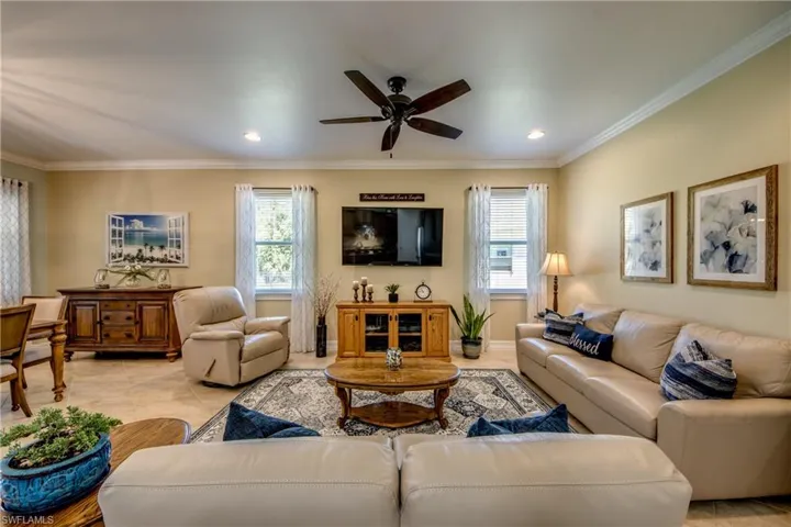 Living room with tile floors, ceiling fan, and crown molding