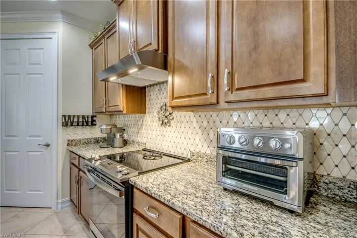 Kitchen with electric range, light stone counters, tasteful backsplash, and light tile floors