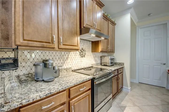 Kitchen featuring crown molding, light stone countertops, backsplash, stainless steel electric range, and light tile floors