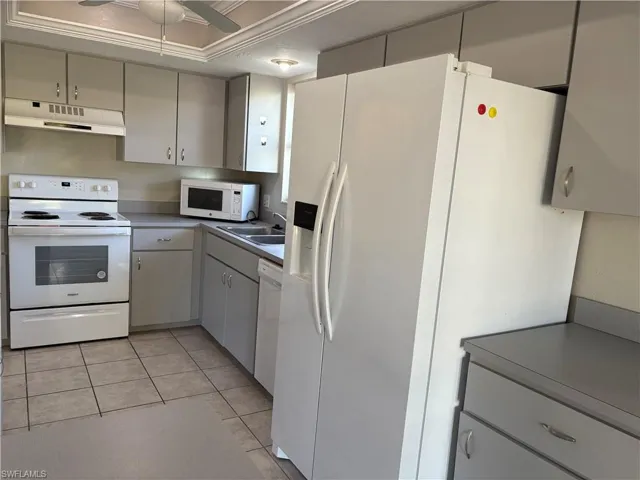 Kitchen with white appliances, light tile patterned floors, under cabinet range hood, a ceiling fan, and gray cabinets