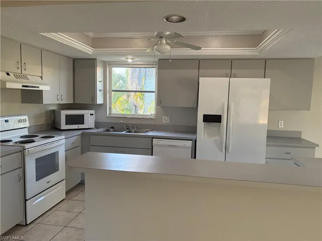 Kitchen featuring white appliances, a raised ceiling, under cabinet range hood, light tile patterned flooring, and crown molding