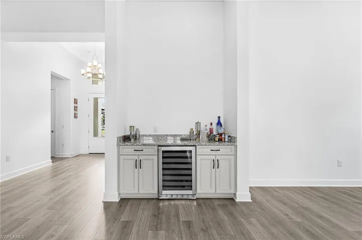 Indoor dry bar with wine cooler, light stone countertops, light wood-style flooring, white cabinets, and pendant lighting