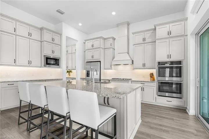 Kitchen with a kitchen breakfast bar, light stone countertops, appliances with stainless steel finishes, tasteful backsplash, and light wood finished floors
