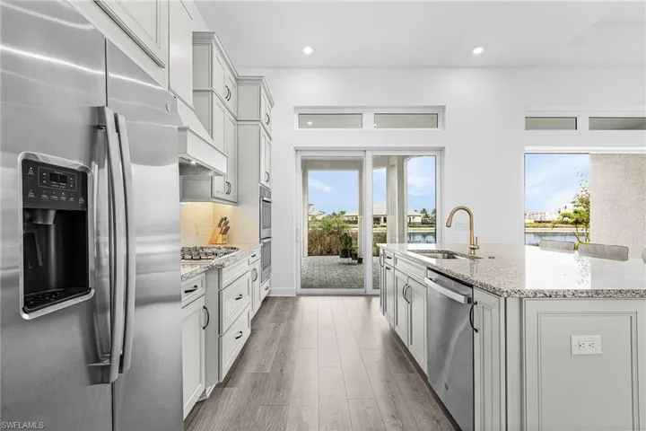 Kitchen featuring stainless steel appliances, light wood-style floors, light stone countertops, a kitchen island with sink, and recessed lighting