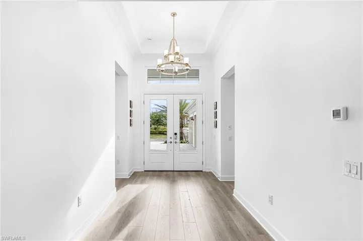 Entrance foyer featuring french doors, crown molding, wood finished floors, a chandelier, and a raised ceiling