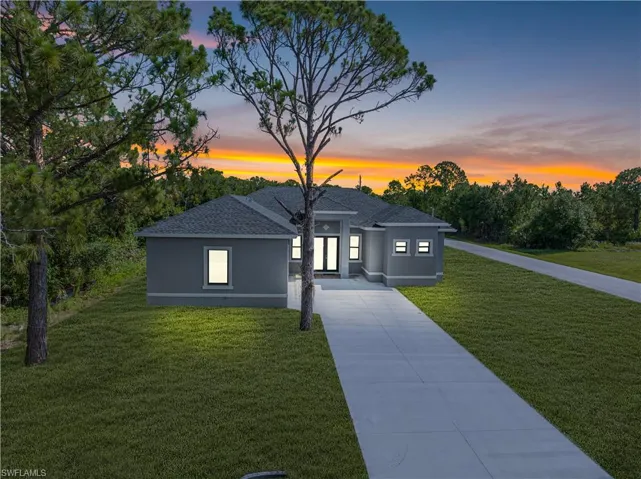 View of front of home with driveway, a yard, stucco siding, and roof with shingles