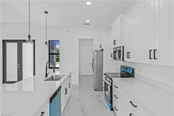 Kitchen with white cabinetry, stainless steel appliances, light stone countertops, pendant lighting, and light marble finish floors