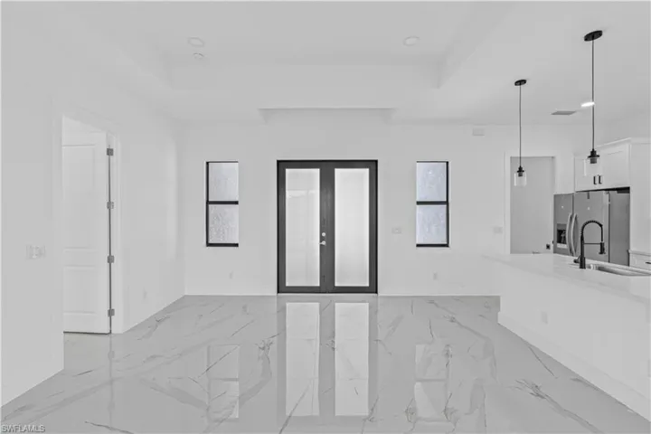 Unfurnished living room featuring french doors, recessed lighting, light marble finish floors, and a raised ceiling