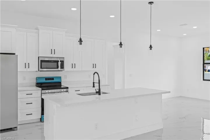 Kitchen featuring stainless steel appliances, white cabinets, light stone counters, decorative light fixtures, and a kitchen island with sink