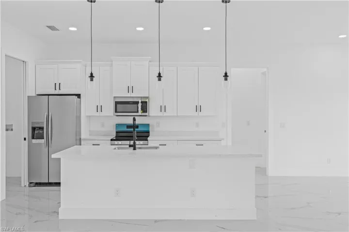 Kitchen featuring stainless steel appliances, white cabinetry, light stone countertops, a kitchen island with sink, and decorative light fixtures