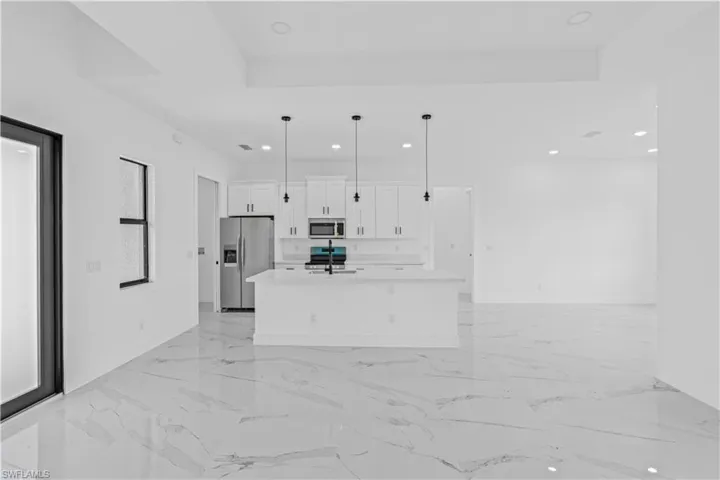 Kitchen featuring white cabinets, stainless steel appliances, an island with sink, open floor plan, and hanging light fixtures