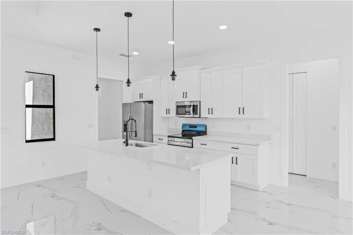 Kitchen featuring stainless steel appliances, white cabinets, light stone counters, a kitchen island with sink, and hanging light fixtures