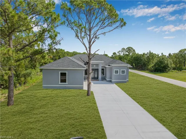 View of front of property with a front yard, stucco siding, driveway, and roof with shingles