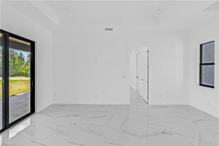 Empty room featuring healthy amount of natural light, a tray ceiling, light marble finish floors, and recessed lighting