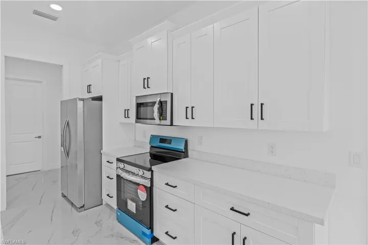 Kitchen with stainless steel appliances, white cabinetry, light stone countertops, light marble finish flooring, and recessed lighting