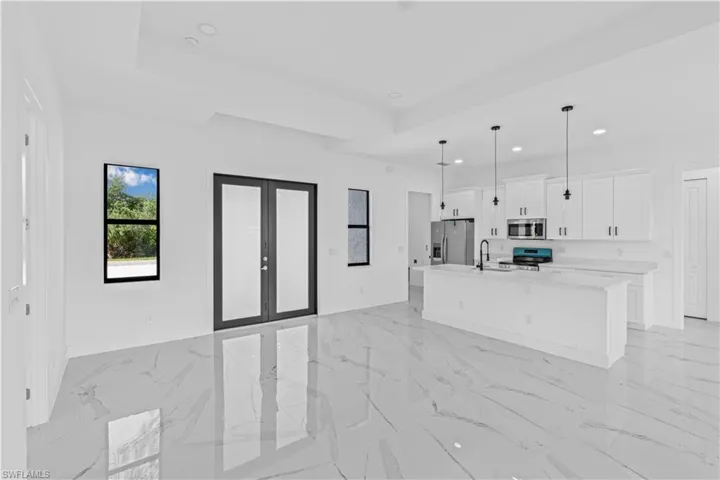 Kitchen featuring french doors, white cabinets, a kitchen island with sink, stainless steel appliances, and open floor plan