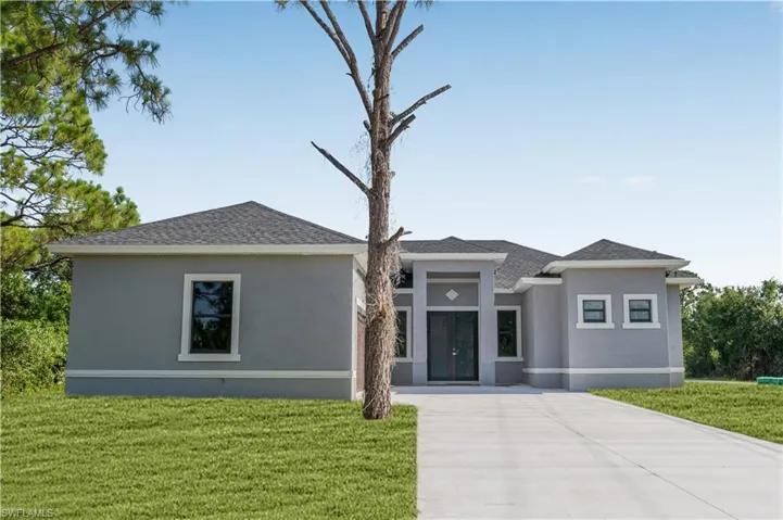 Prairie-style house featuring a front yard, stucco siding, a shingled roof, and concrete driveway