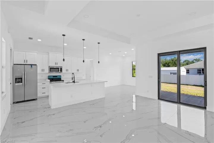 Kitchen featuring stainless steel appliances, white cabinets, a center island with sink, open floor plan, and a raised ceiling