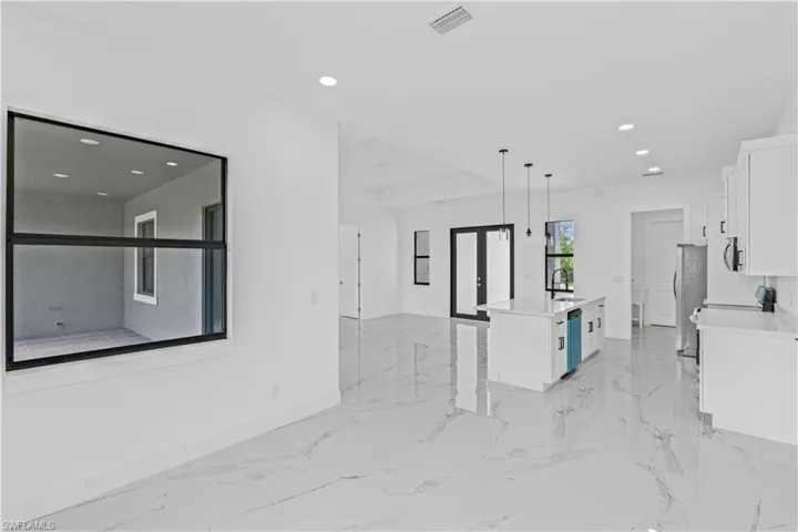 Kitchen featuring open floor plan, white cabinets, a center island with sink, light stone counters, and hanging light fixtures