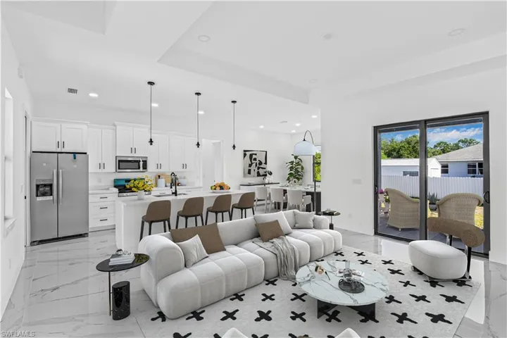 Living area with a tray ceiling, recessed lighting, and light marble finish floors