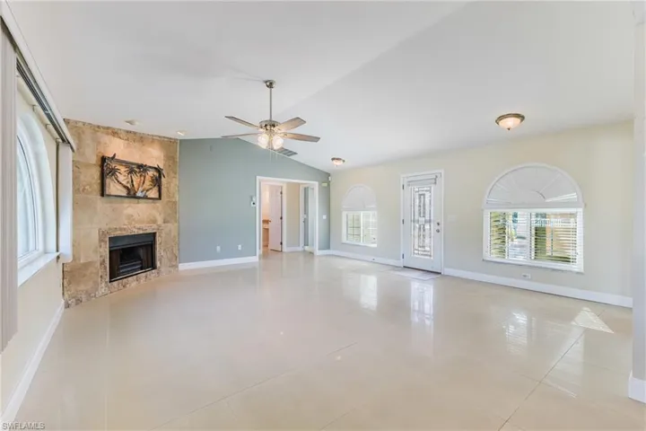 Unfurnished living room featuring a tile fireplace, light tile patterned floors, a ceiling fan, and lofted ceiling