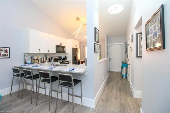 Kitchen with white cabinetry, light hardwood / wood-style floors, lofted ceiling, backsplash, and a kitchen bar