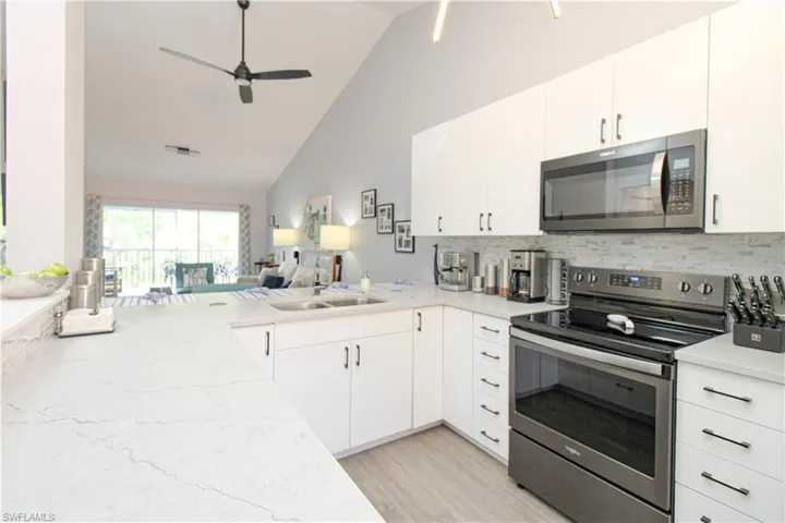 Kitchen with ceiling fan, stainless steel appliances, light wood-type flooring, backsplash, and high vaulted ceiling