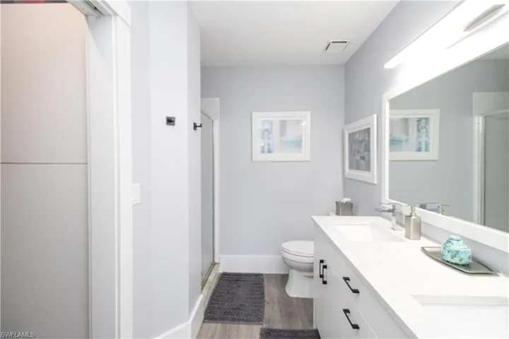 Bathroom featuring dual bowl vanity, an enclosed shower, toilet, and wood-type flooring