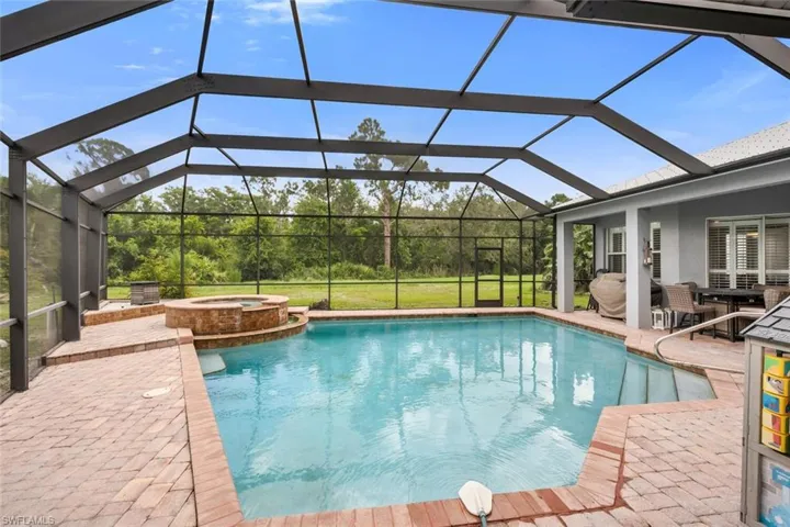 View of swimming pool with a patio area, a pool with connected hot tub, and glass enclosure