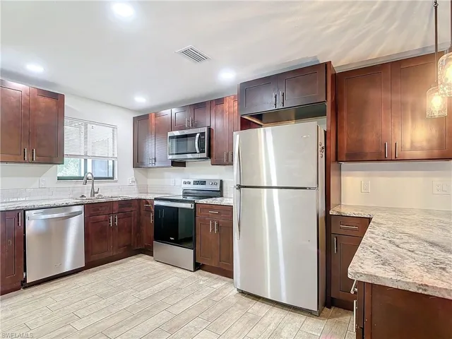 Kitchen with sink, light stone counters, light hardwood / wood-style floors, and stainless steel appliances