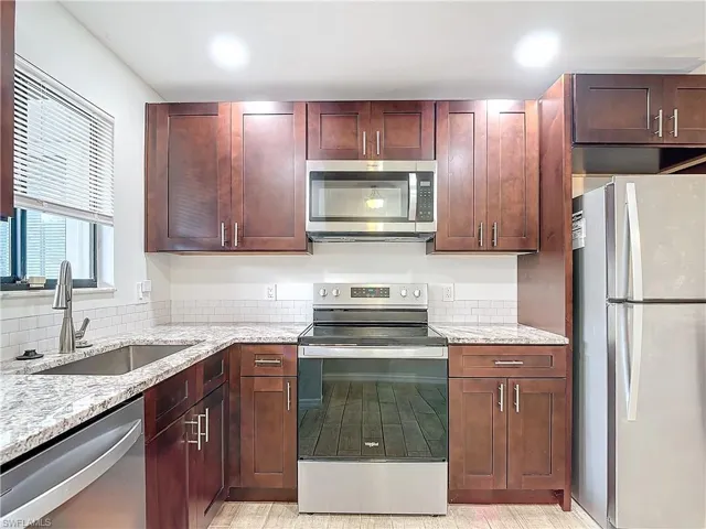 Kitchen with decorative backsplash, light stone countertops, sink, and stainless steel appliances