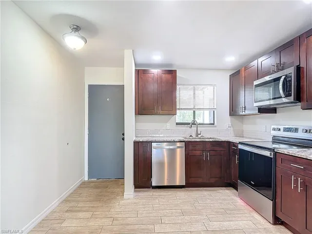 Kitchen with stainless steel appliances, sink, light stone counters, and light hardwood / wood-style flooring