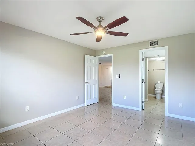 Unfurnished bedroom featuring light tile patterned floors, ceiling fan, and ensuite bathroom