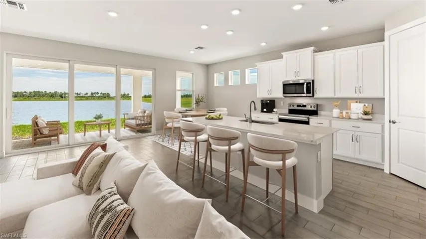 Sliding glass doors opening to a large patio, modern kitchen with white cabinetry, stainless steel appliances, a center island with bar seating, and wood-finish flooring