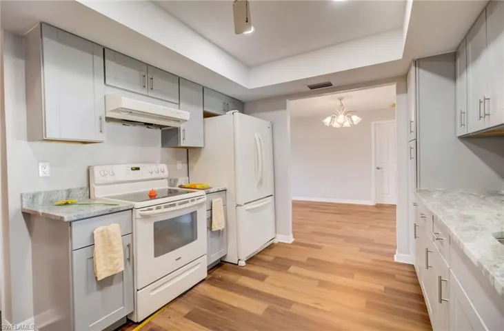 Kitchen featuring a raised ceiling, white appliances, a chandelier, and light hardwood / wood-style flooring