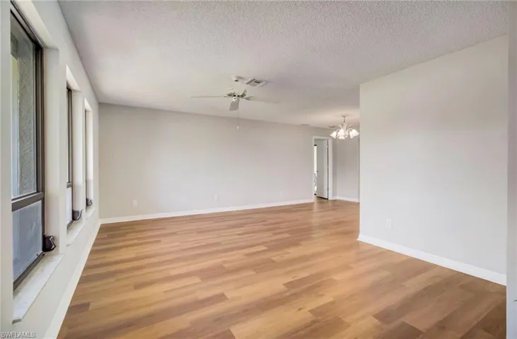 Living room featuring a textured ceiling, ceiling fan with notable chandelier, and warm wood-style floors
