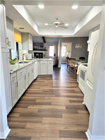 Kitchen featuring white cabinets, ceiling fan with notable chandelier, white appliances, dark hardwood / wood-style flooring, and sink