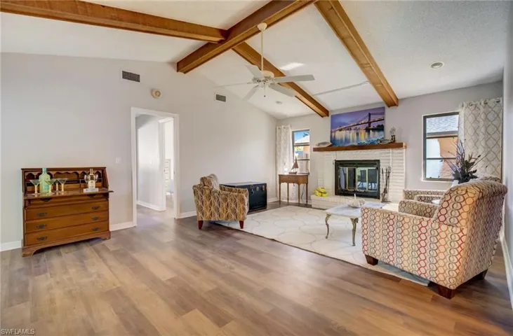 Family room with a textured ceiling, a brick fireplace, wood-style flooring, ceiling fan, and vaulted ceiling with beams