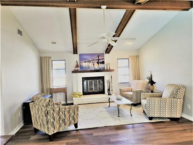 Living room featuring a fireplace, hardwood / wood-style floors, ceiling fan, and vaulted ceiling with beams