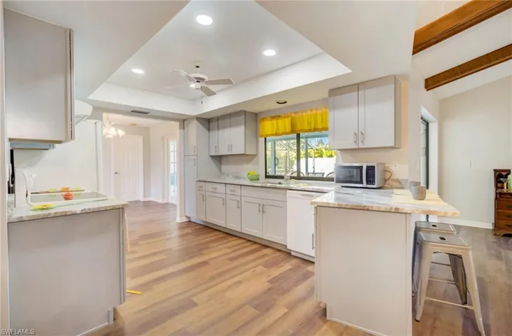 Kitchen with light hardwood / wood-style flooring, a kitchen bar, dishwasher, light stone countertops, and ceiling fan