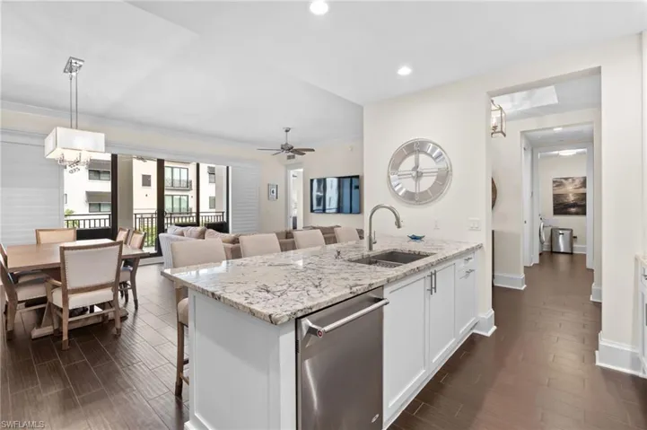 Kitchen featuring a kitchen bar, light stone countertops, white cabinets, stainless steel dishwasher, and decorative light fixtures
