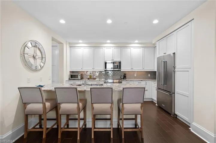 Kitchen with a breakfast bar, tasteful backsplash, appliances with stainless steel finishes, light stone counters, and white cabinets