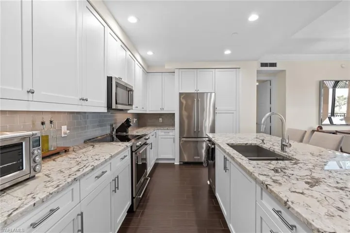 Kitchen with appliances with stainless steel finishes, light stone countertops, tasteful backsplash, recessed lighting, and white cabinetry