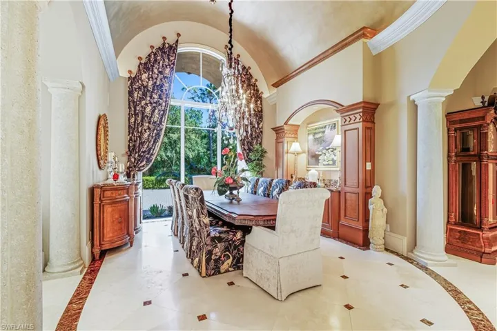 Dining space featuring decorative columns, inlaid floor details, high vaulted ceiling, crown molding, and arched walkways