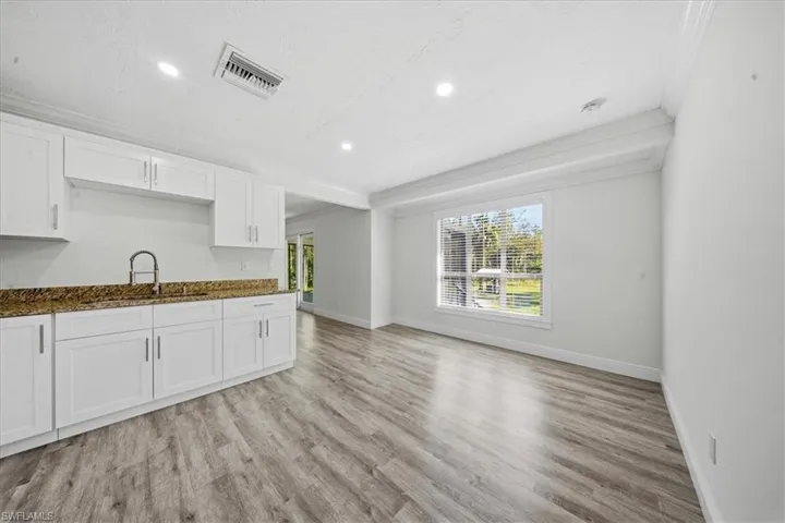 Kitchen with white cabinetry, ornamental molding, light wood finished floors, recessed lighting, and dark stone counters