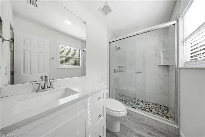 Bathroom featuring vanity, a marble finish shower, and light wood-style floors
